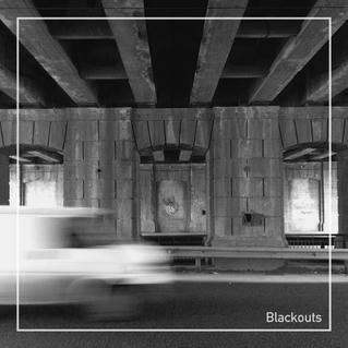 black and white photo of a bridge-like structure with a blurred white van passing by in the foreground